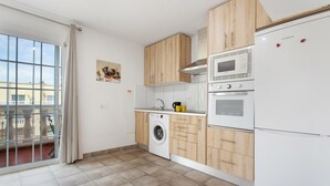 Een moderne keuken met houten kastjes, een wasmachine, een magnetron en een koelkast.