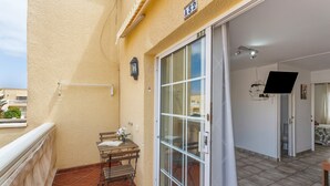 Een balkon met een tafel, stoelen, een schuifpui en een aan de muur bevestigde televisie.