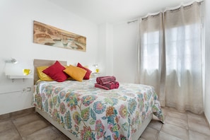 Une chambre à coucher avec une couvre-lit à motifs floraux, un tableau au mur et une fenêtre avec des rideaux.