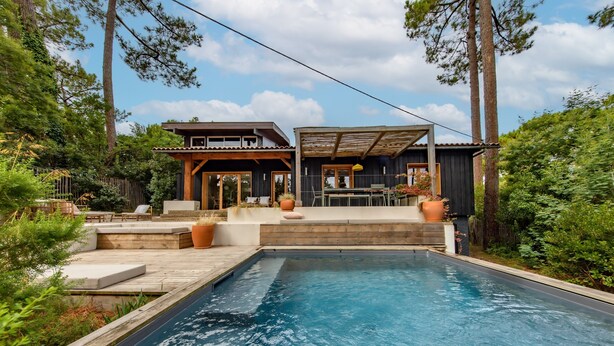 Ein modernes Haus mit Schwimmbad, Holzterrasse und Gartenmöbeln.