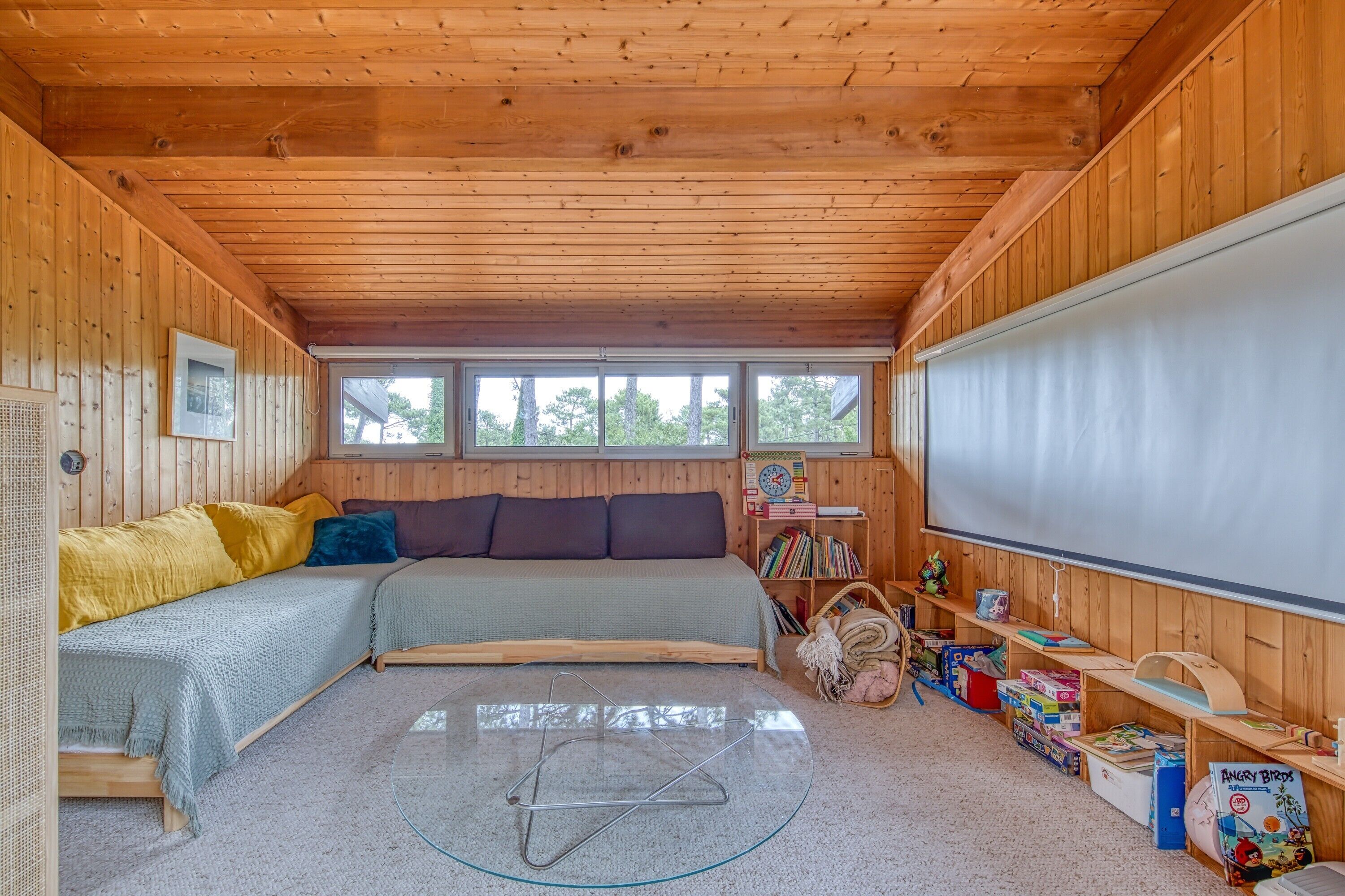 L’intérieur chaleureux d’un chalet comprend un lit, une petite table, une bibliothèque et un écran de projection.