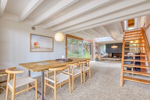 Un vaste espace de vie comprenant une table à manger en bois, des chaises, un escalier et une grande fenêtre.