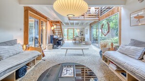 Ein modernes Interieur mit einer großen Holztreppe, einer hängenden Leuchte und Blick durch hohe Fenster.