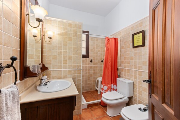 A bathroom with a sink, toilet, shower, and a framed sign on the wall.