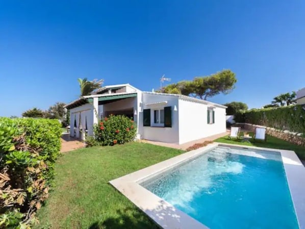 Una propiedad residencial con piscina, terraza cubierta y césped bien cuidado.