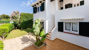 Un bâtiment à deux étages, avec une façade blanche, des volets verts et une terrasse carrelée.