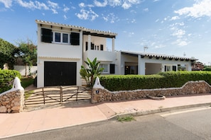 Una casa de dos pisos con un muro de piedra, un portón negro y un camino de entrada pavimentado.