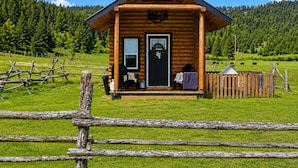 A wooden cabin with a front porch, a door with a wreath, and a fenced yard.