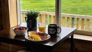 A breakfast table with a bowl of fruit, toast, scrambled eggs, bacon, a mug, and a glass of orange juice.