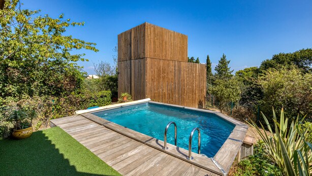 Una piscina rectangular con cubierta de madera y barandillas de metal, rodeada de abundante vegetación y una estructura de madera alta.
