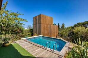A rectangular pool with a wooden deck and metal railings, surrounded by lush greenery and a tall wooden structure. - Holiday Home 'Greenkub' with Shared Pool, Wi-Fi and Air Conditioning (Générac)