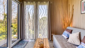 Una habitación con puerta corredera de vidrio, piso de madera, un sofá con cojines y una mesa con una vela.