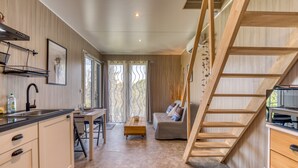 Una cocina moderna con escalera de madera, comedor y sofá en una habitación con paredes de madera y ventanas amplias.