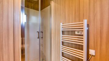 Un baño moderno con cabina de ducha de vidrio, toallero blanco y paneles de madera.