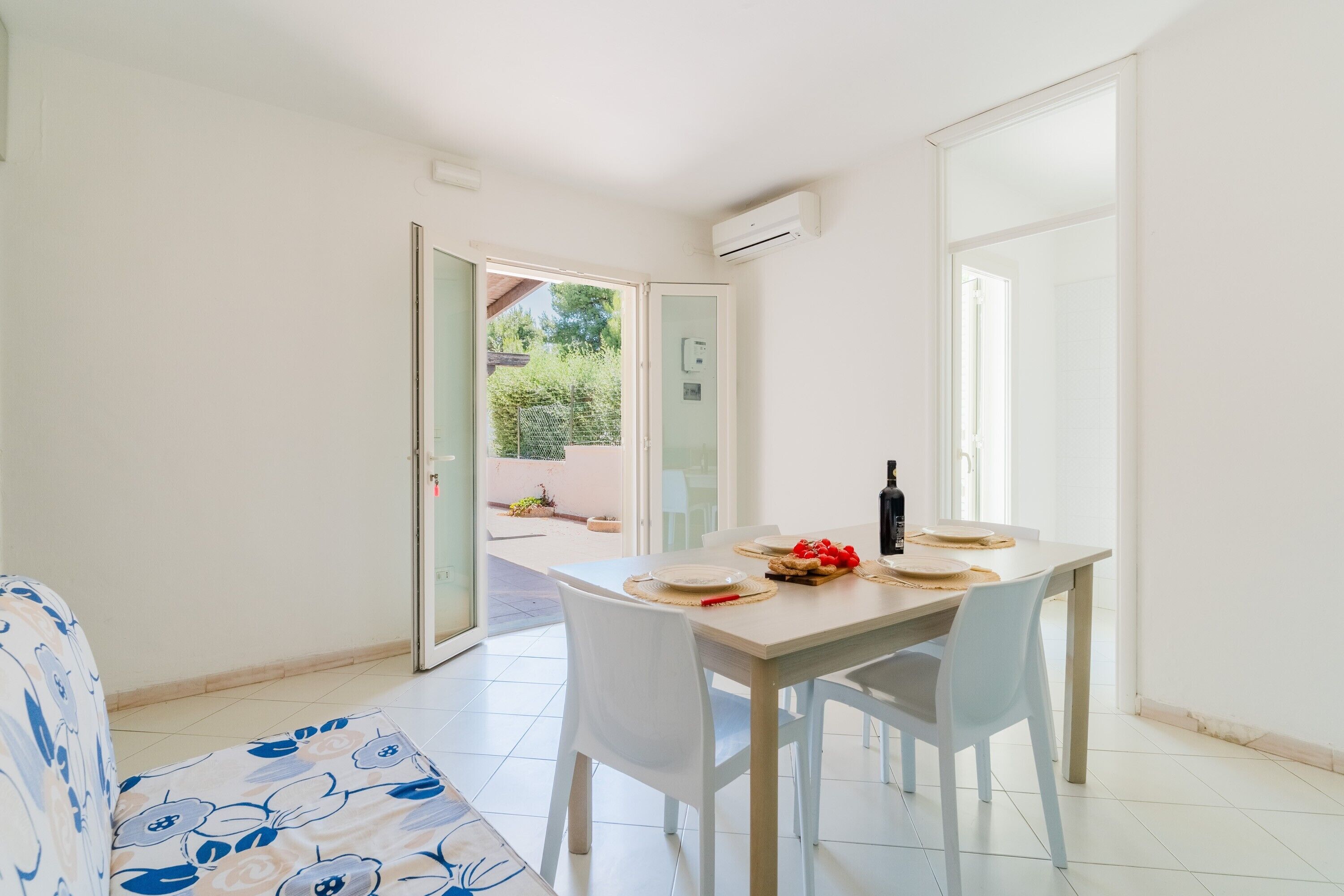 Un comedor con una mesa lista para dos personas, un sofá y un ventanal corredero que da a un espacio exterior.