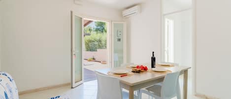 Un comedor con una mesa lista para dos personas, un sofá y un ventanal corredero que da a un espacio exterior.