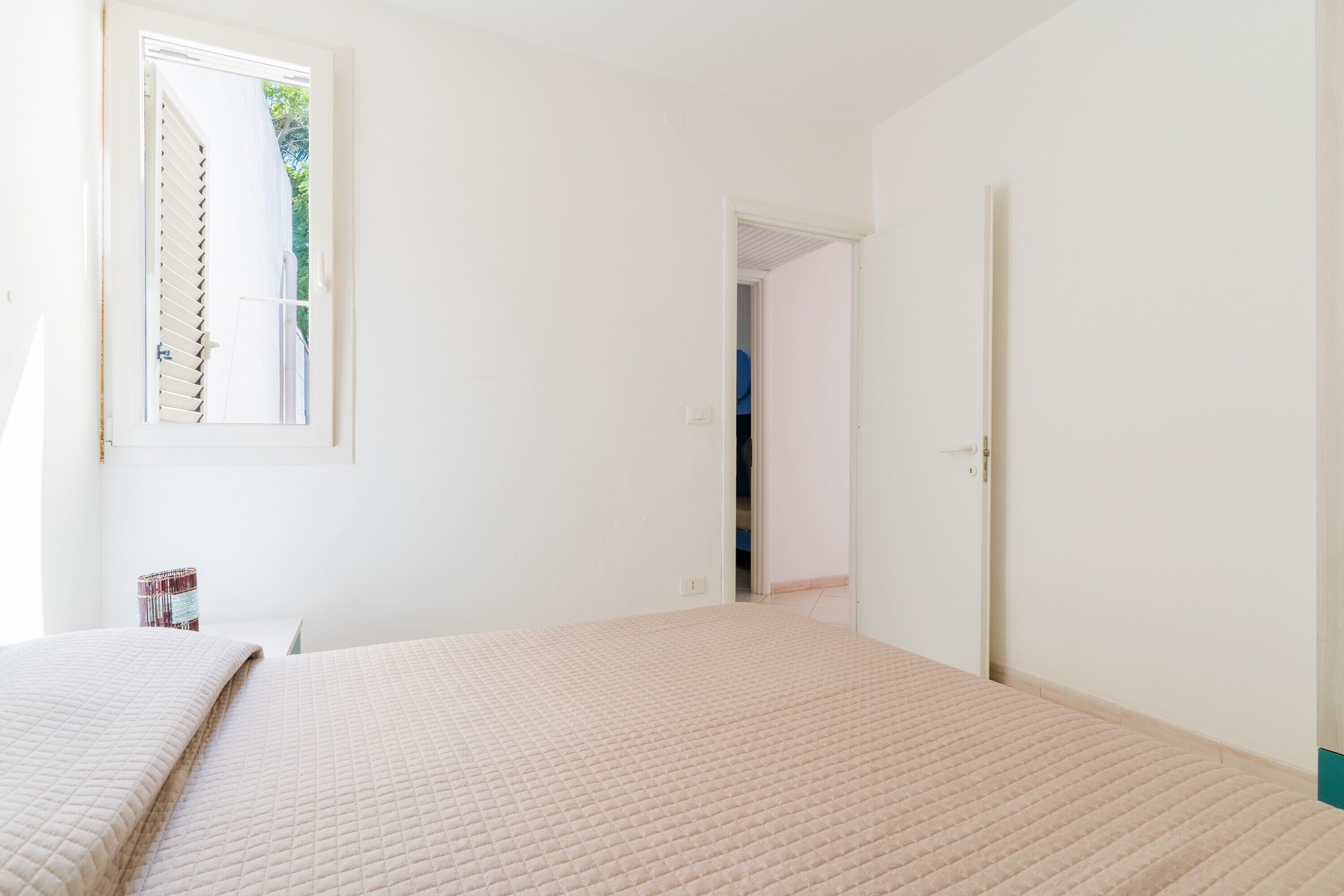 A room with a bed, a window, and a door leading to another room.
