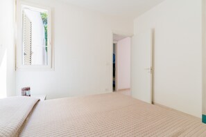 A room with a bed, a window, and a door leading to another room.