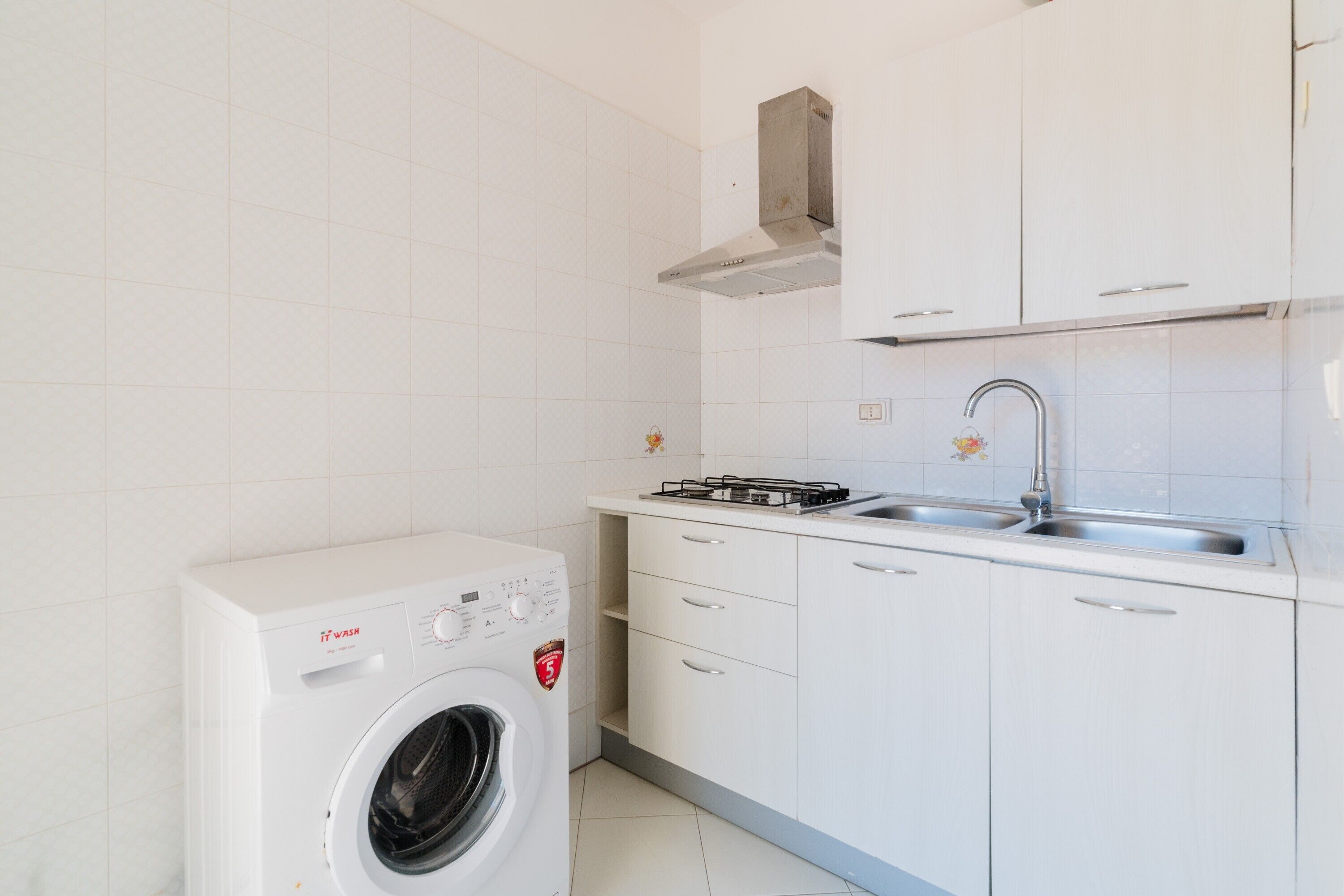A compact kitchen with a built-in washing machine, a gas stove, and a stainless steel sink.