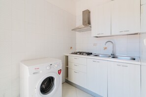 Ett kompakt kök med en inbyggd tvättmaskin, en gasspis och en diskho i rostfritt stål.