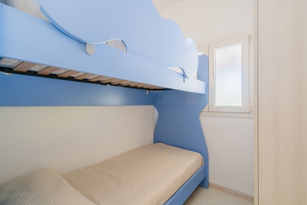 A bunk bed with a mattress, a window, and a wall with a unique design.