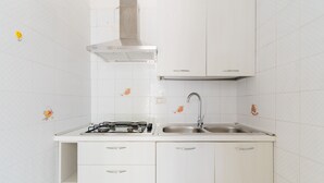 Una cocina con armarios blancos, estufa a gas, un fregadero y una campana extractora de acero inoxidable.