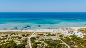 Vista aérea de una playa con cielo despejado, una orilla arenosa y un edificio con techo azul.
