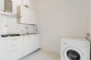 A compact kitchen with a built-in washing machine, white cabinets, and a stainless steel sink. - Holiday Home 'Villetta Pinetata 452' with Private Terrace and Air Conditioning (UGENTO)