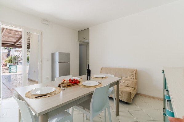 A dining area with a table set for two, a sofa, and a refrigerator.