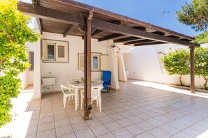 Eine überdachte Terrasse mit Fliesenboden, einem weißen Tisch mit Stühlen und einem blauen Sessel.