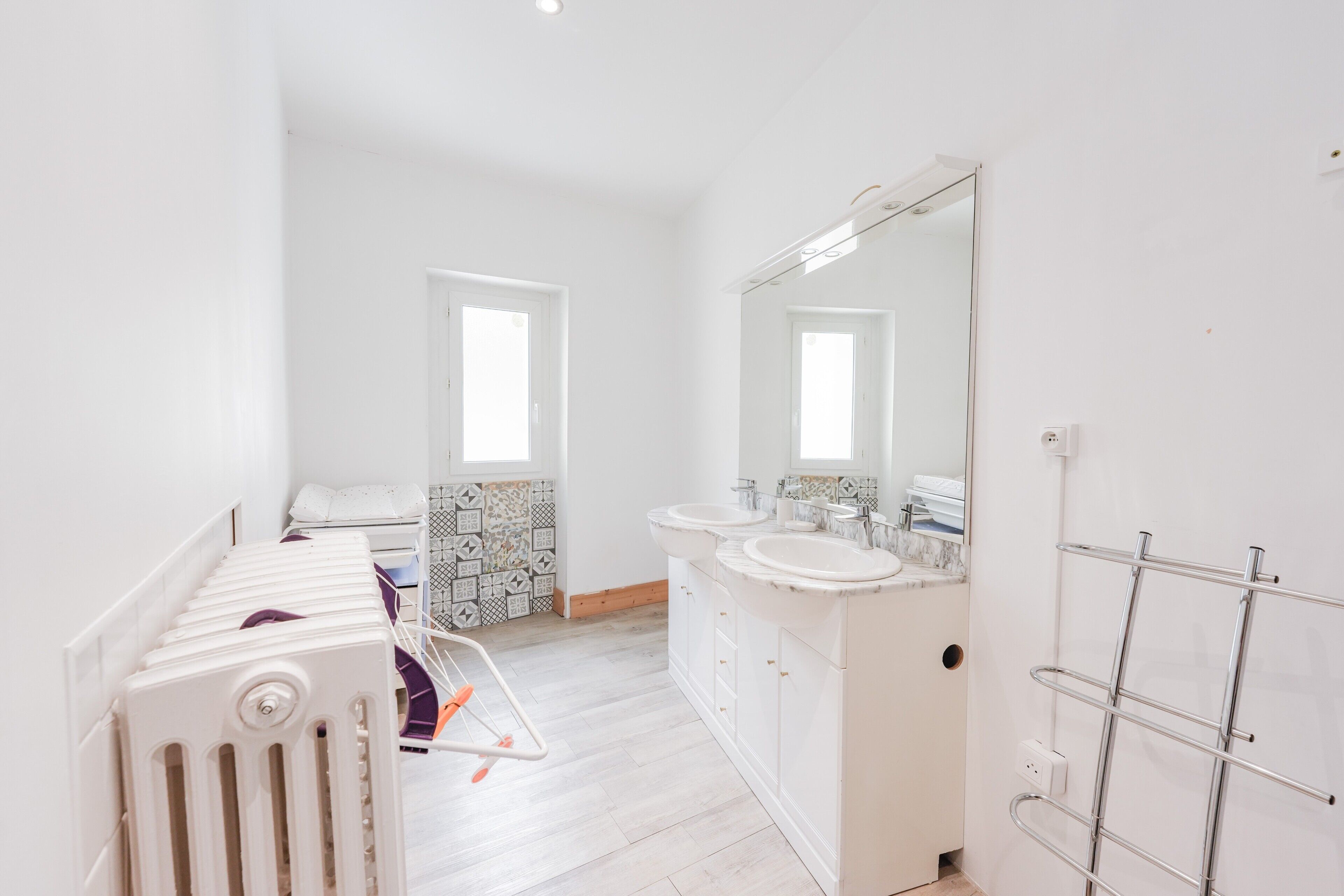 A modern bathroom with two sinks, a large mirror, and a radiator.