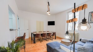Uma sala de estar moderna com sofá, mesa de jantar, cadeiras, televisão e planta.