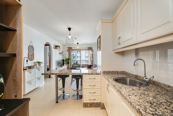 A kitchen with a granite countertop, stainless steel sink, and bar stools.
