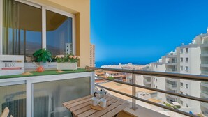 A balcony with a table, chairs, a window with a view of the city, and a sign labeled 'BOX'. - Vacation Apartment 'Apto Sol Paraiso Sunset View' with Shared Pool, Private Terrace and Wi-Fi (Adeje)