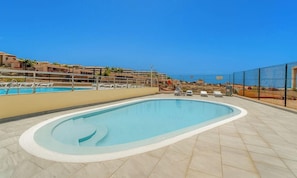 A swimming pool with a tiled deck, a fenced area, and a view of the sea.