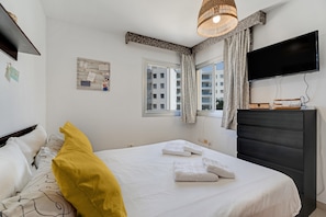 A hotel room with a bed, a television, a window with curtains, and a wall-mounted TV.