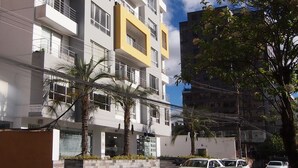 Un immeuble résidentiel à plusieurs étages, doté de balcons, d’une entrée sécurisée et d’un espace de stationnement avec des voitures.