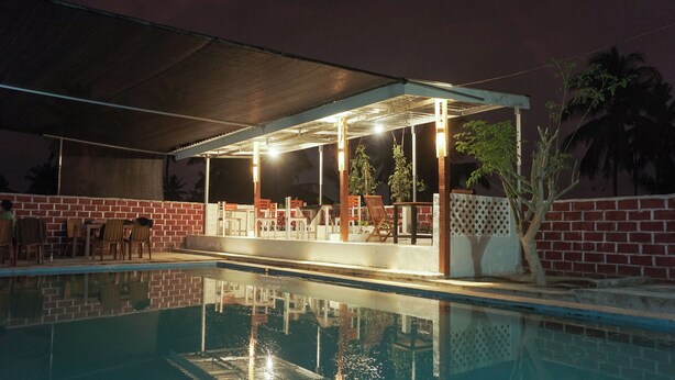 An outdoor pool area with a covered seating area, brick walls, and palm trees. - Rinjani Terrace Cottage (Kotaraja)