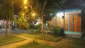 A nighttime view of a building with a paved entrance, surrounded by trees and a well-lit pathway. - Rinjani Terrace Cottage (Kotaraja)