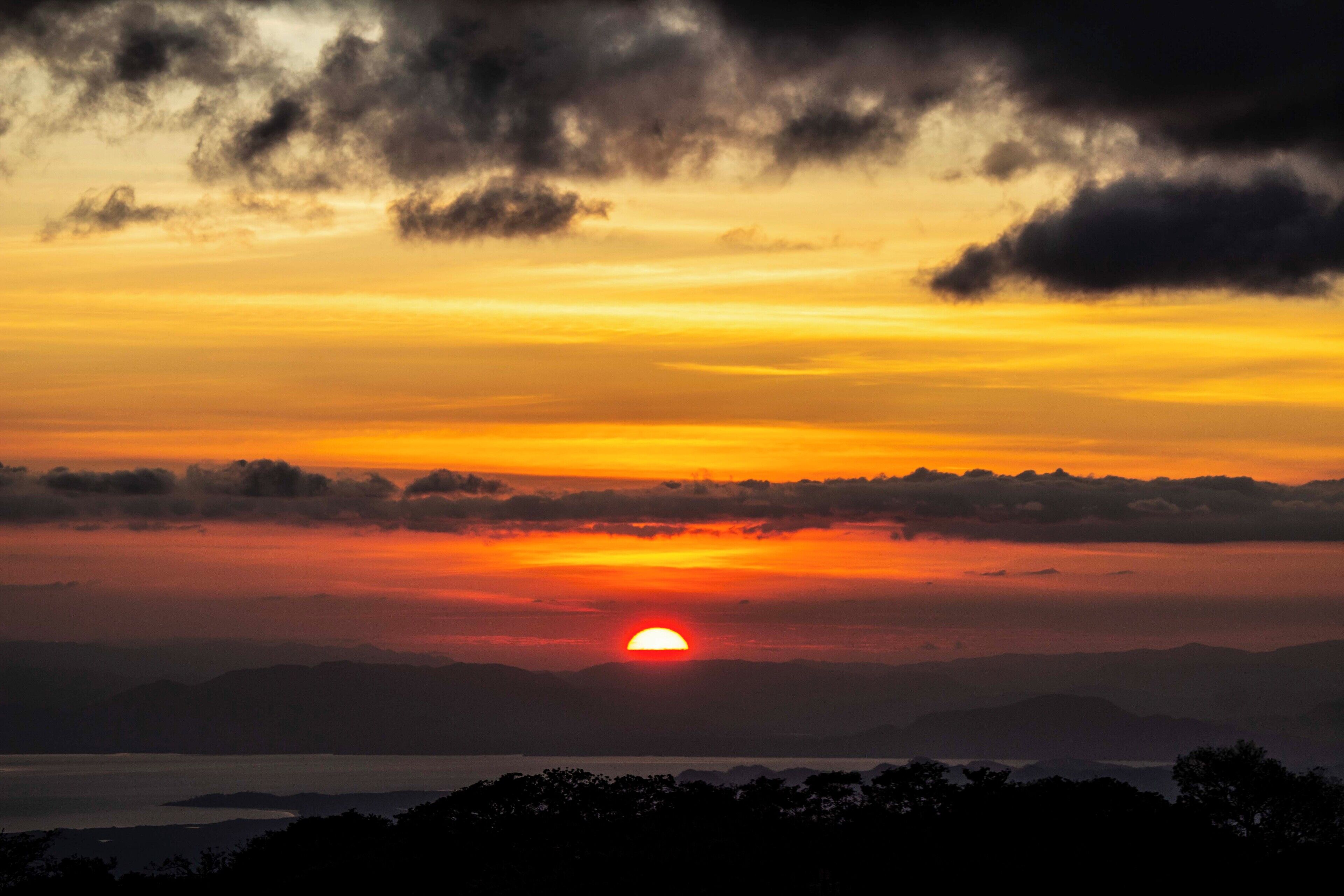 A sunset over a mountainous landscape with a clear view of the sun setting behind the hills.