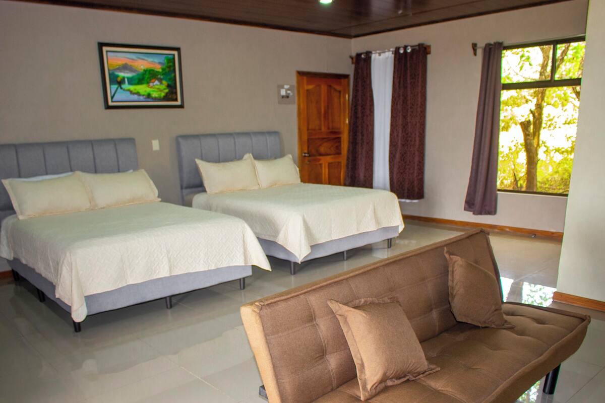 A hotel room with two beds, a sofa, a painting on the wall, and a window with curtains.