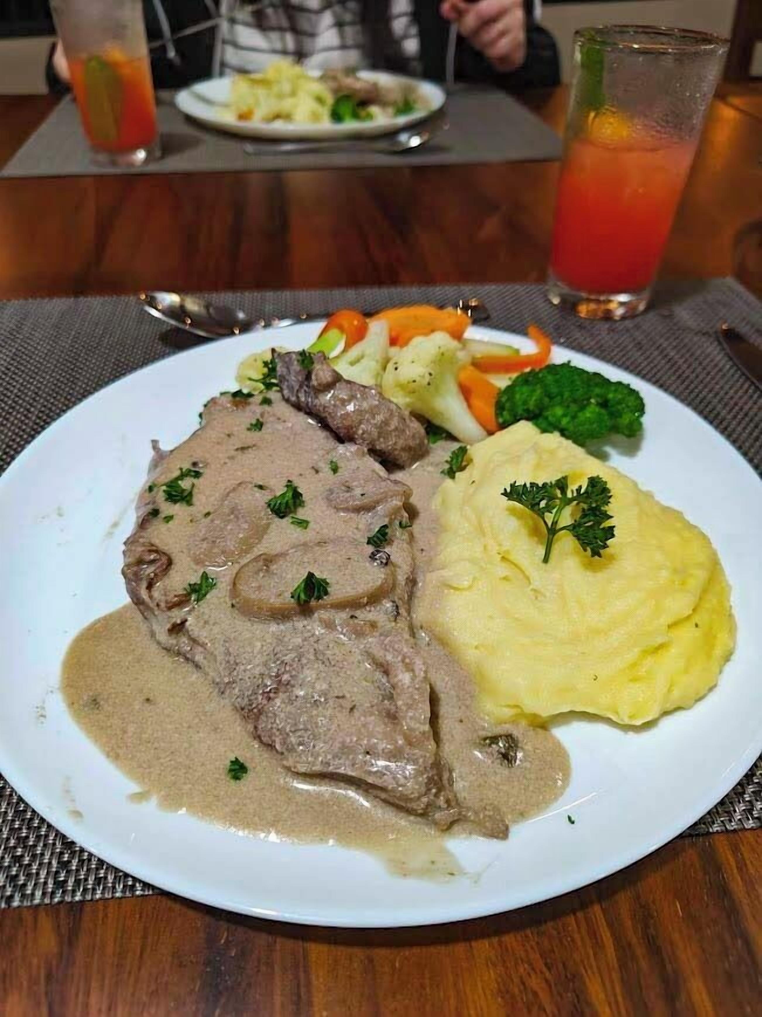 A plate of food with a slice of meat, mashed potatoes, and vegetables.