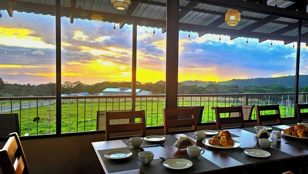 Un coin repas avec une table mise pour le petit-déjeuner, offrant une vue sur un paysage verdoyant et des collines au coucher du soleil.