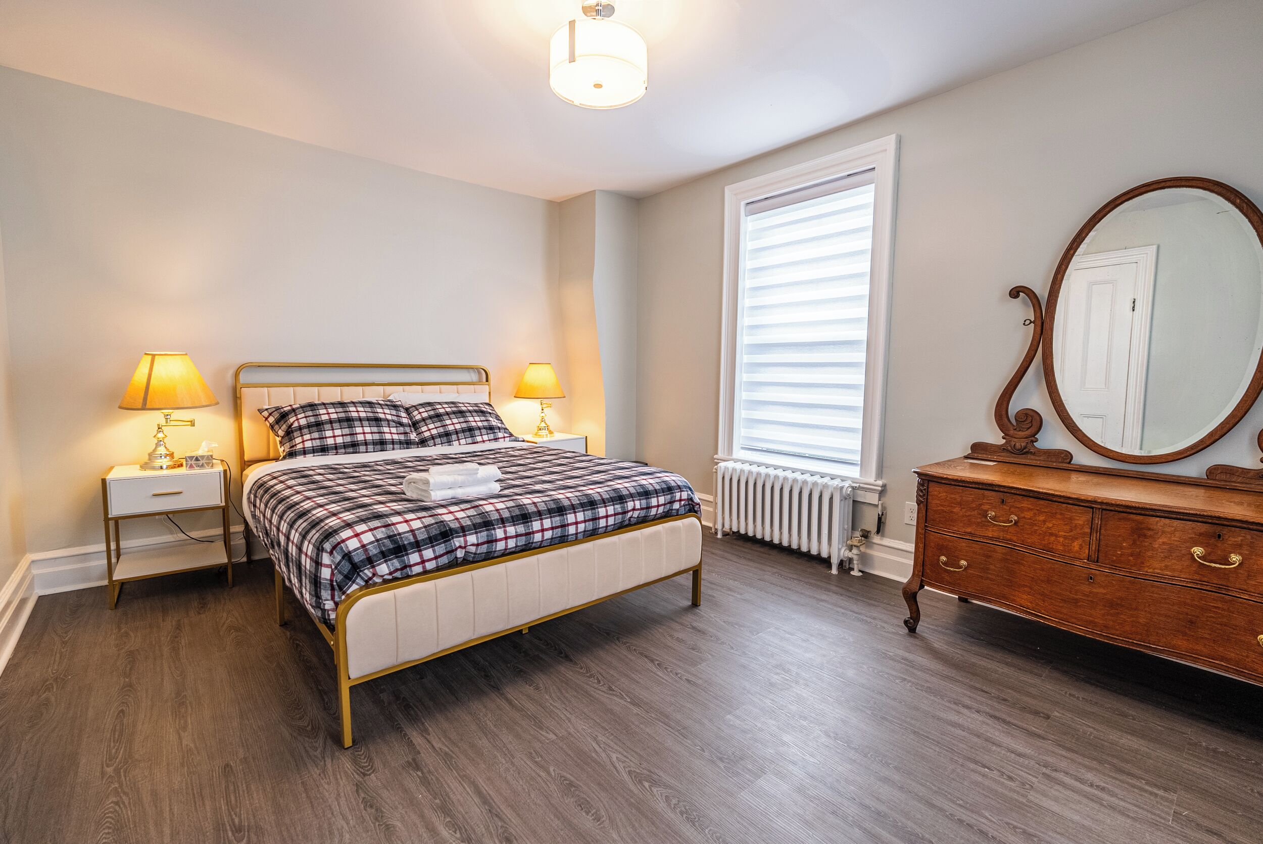 Un dormitorio con cama, mesitas de noche, cómoda, espejo y ventana con persianas.