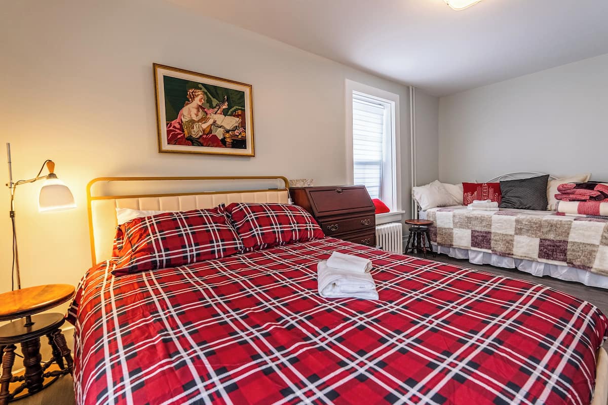 A bedroom with a large bed, a smaller bed, a nightstand, a lamp, and a painting on the wall.