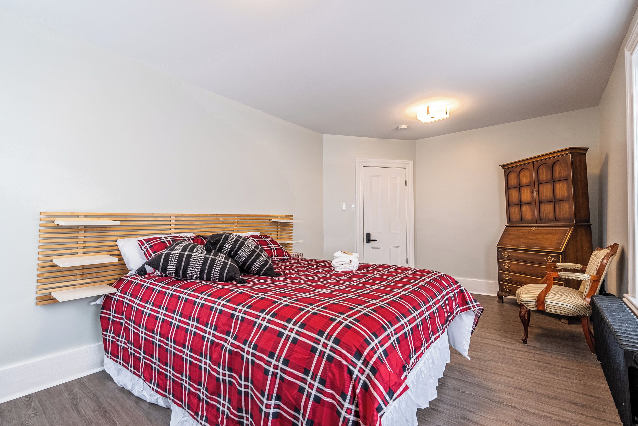 A bedroom with a bed, wooden headboard, a dresser, and a chair.