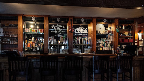 A bar with wooden bar counters and shelves stocked with bottles and glasses. - ATLANTIC HOTEL (Alexandria)