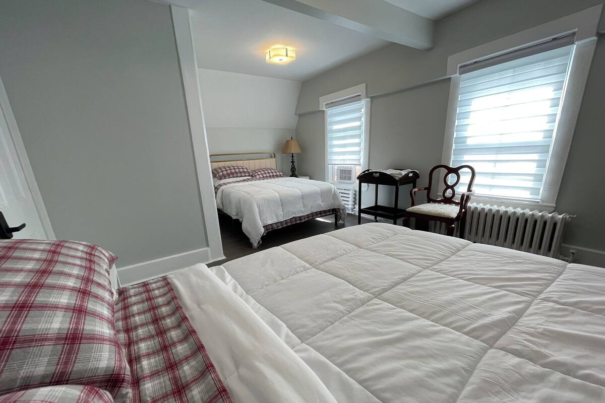 A bedroom with two beds, a chair, a radiator, and a window with blinds.