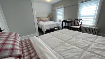 Un dormitorio con dos camas, una silla, un radiador y una ventana con persianas.