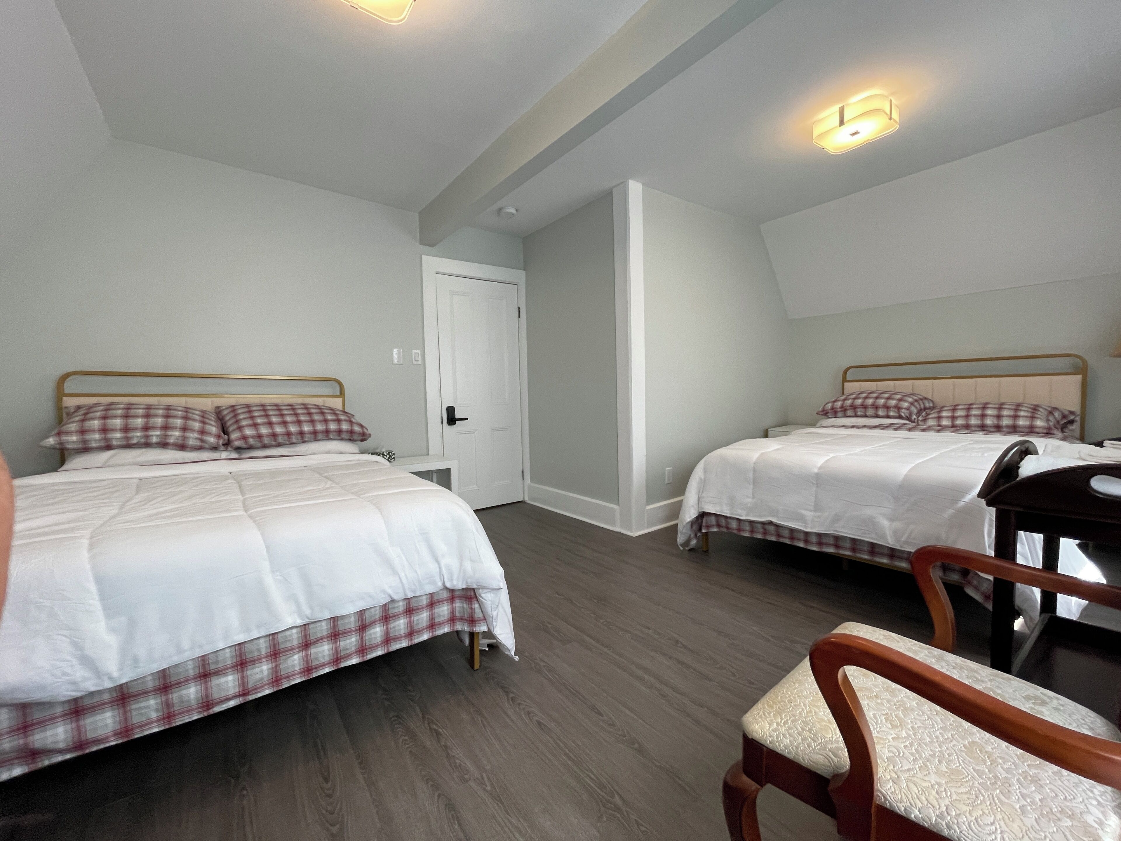 A bedroom with two beds, a wooden chair, and a white door.